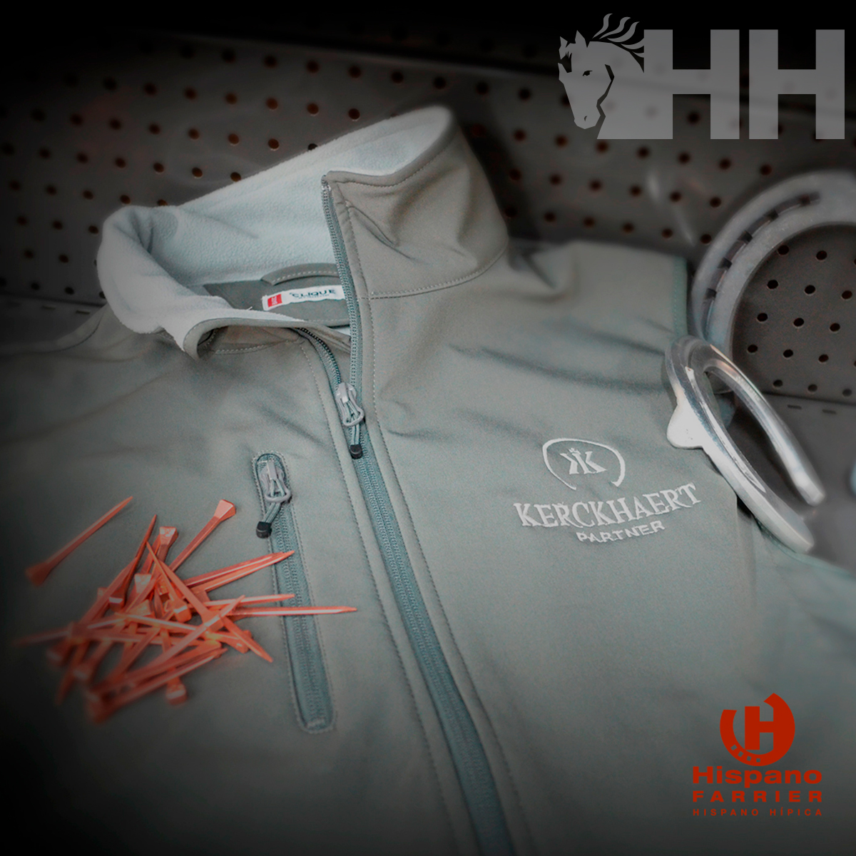 Casaco cinza claro com bordado na frente sobre superfície perfurada ao lado de pegs cor de rosa e cabos brancos.