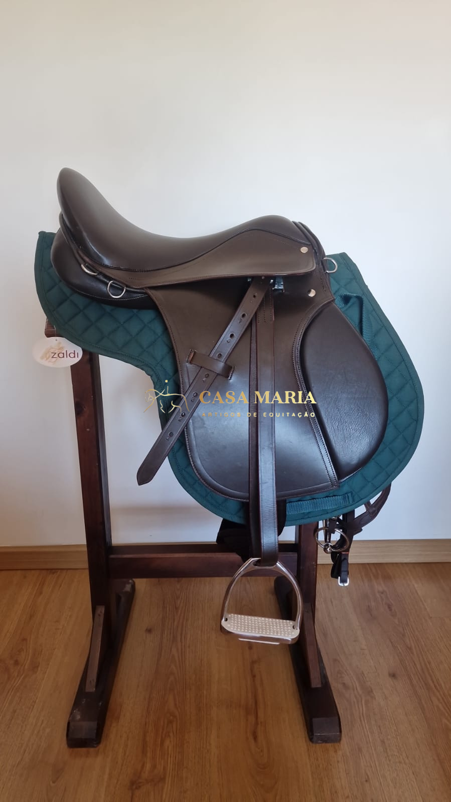 Sela de equitação castanha sobre manta verde em suporte de madeira