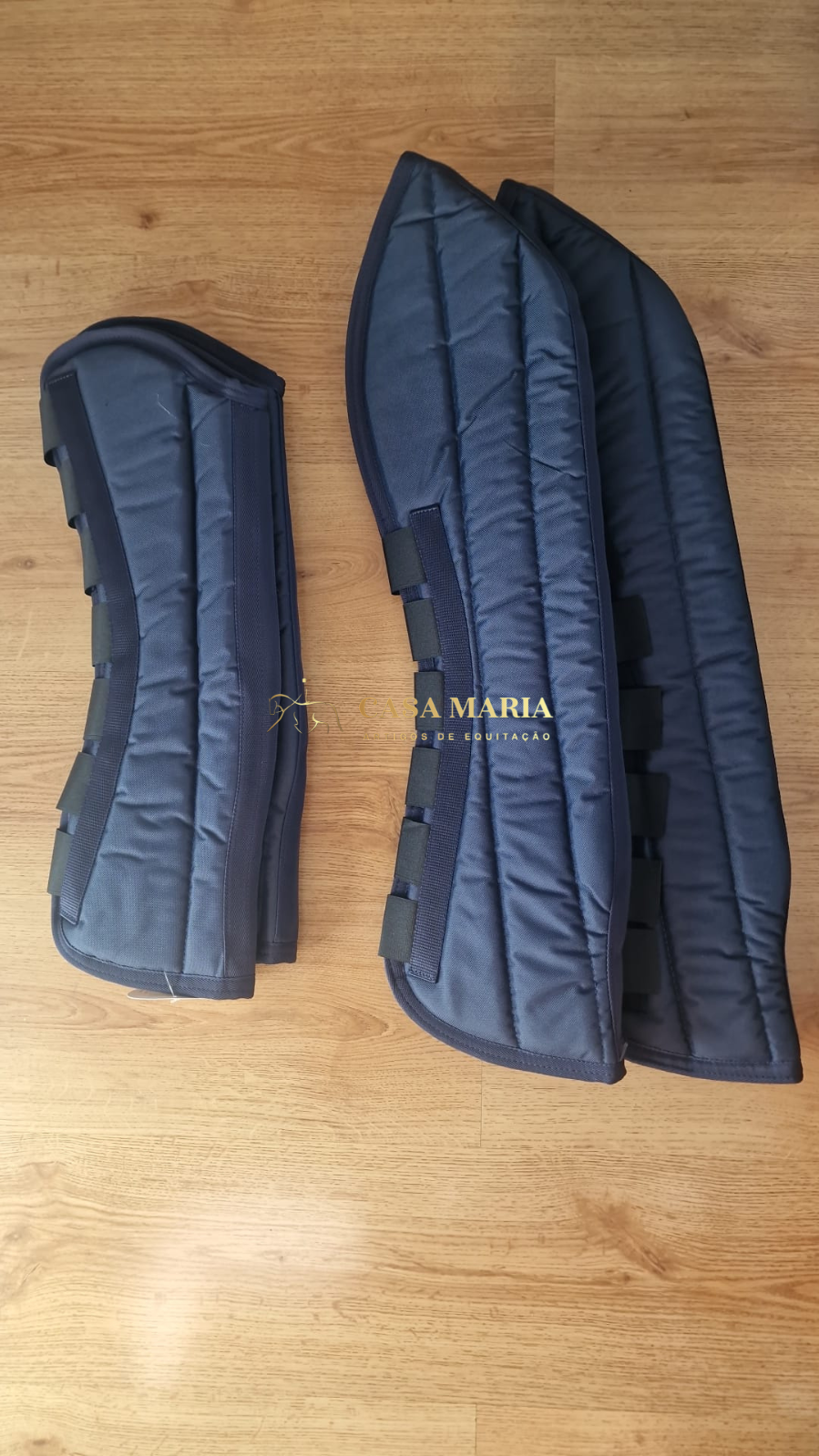 Protetores acolchoados azuis escuros para equitação com tiras de velcro sobre piso de madeira
