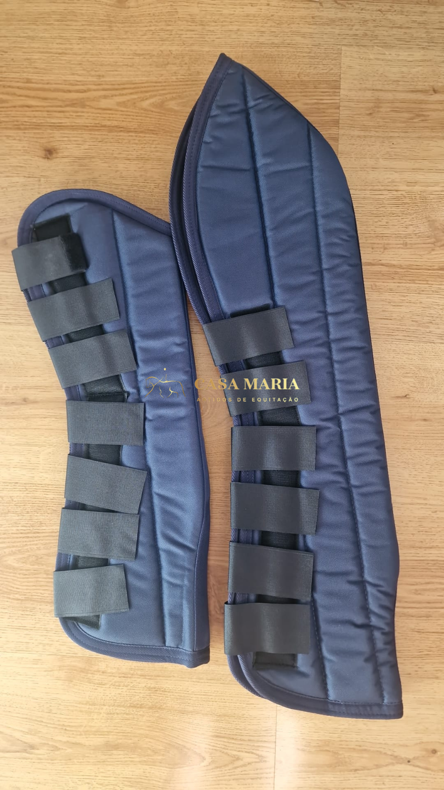 Protetores azuis escuros para patas de cavalos com tiras de velcro pretas sobre piso de madeira