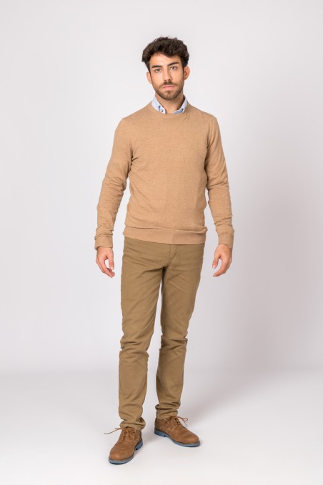 Homem com camisola castanha, camisa azul, calças bege e sapatos castanhos em fundo branco.