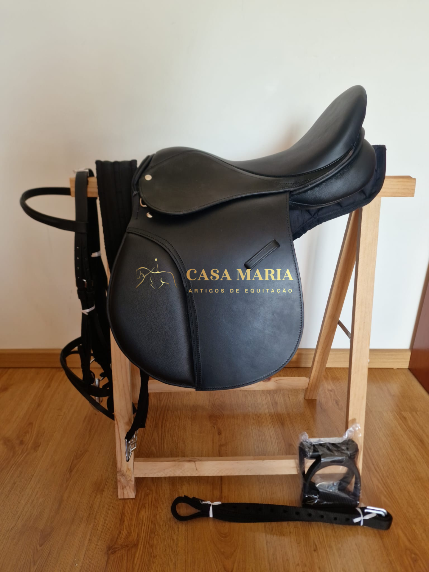 Sela de equitação preta em couro sobre suporte de madeira com acessórios e rédeas pretas.