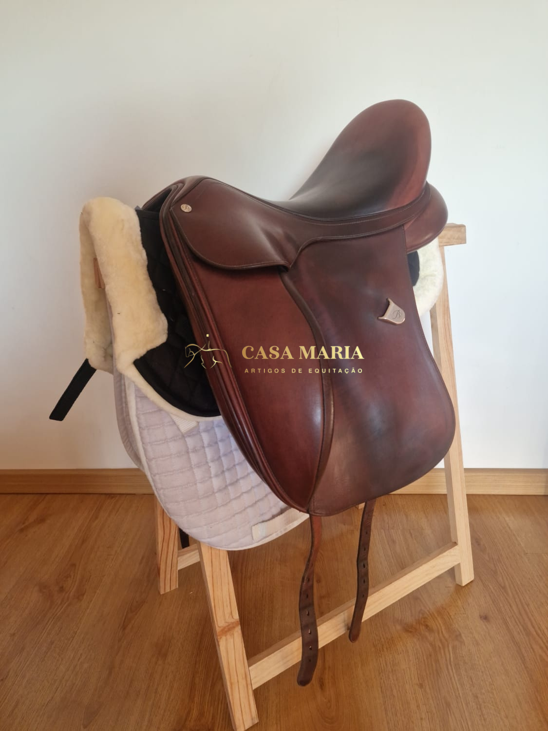 Sela de equitação em couro castanho sobre manta branca em suporte de madeira