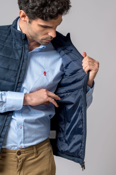 Homem a mostrar interior de colete azul-escuro acolchoado sobre camisa azul clara com bordado vermelho