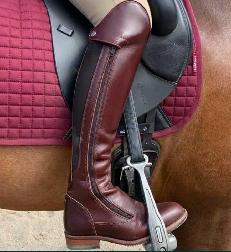 Bota de equitação castanha em sela preta sobre cavalo castanho