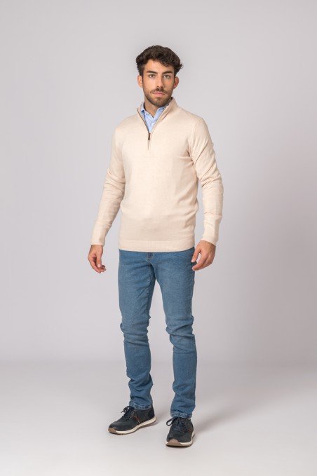 Homem com camisola bege de gola rabe, camisa azul clara e jeans azuis