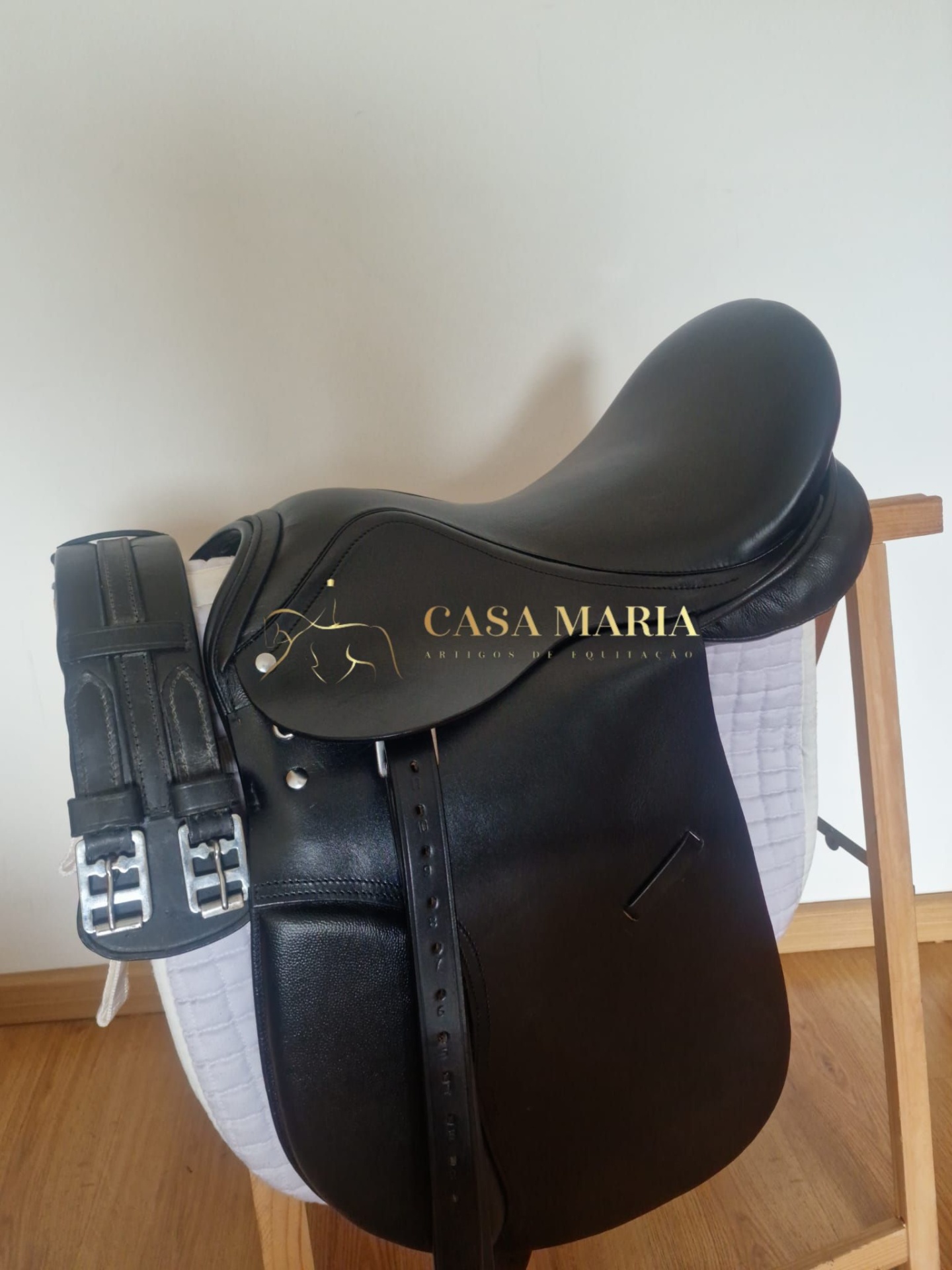 Sela de equitação preta em couro com logo dourado sobre faixa branca acolchoada