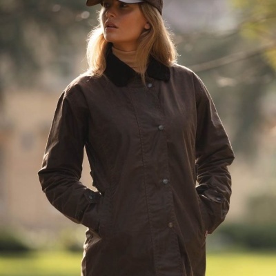 Mulher a usar casaco impermeável castanho escuro com gola preta, ao ar livre.