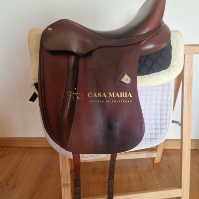 Sela de cavalo de couro castanho pendurada em suporte de madeira com manta acolchoada branca e negra