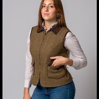 Mulher com colete castanho, camisa xadrez branca e jeans azul, fundo cinzento