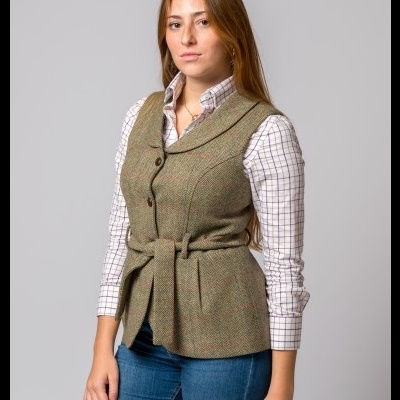 Colete feminino de tweed verde com cinto e botões, camisa quadriculada branca e castanha, jeans azul