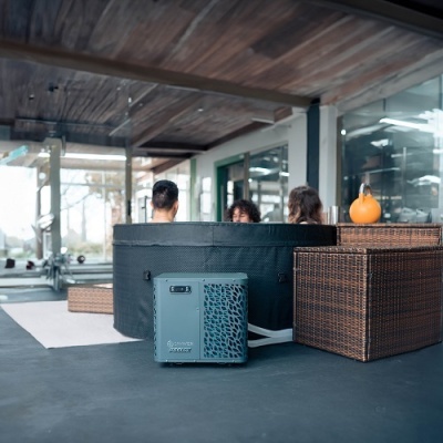 Spa circular preto com unidade de controlo cinza, terraço com teto de madeira e mobiliário de vime.