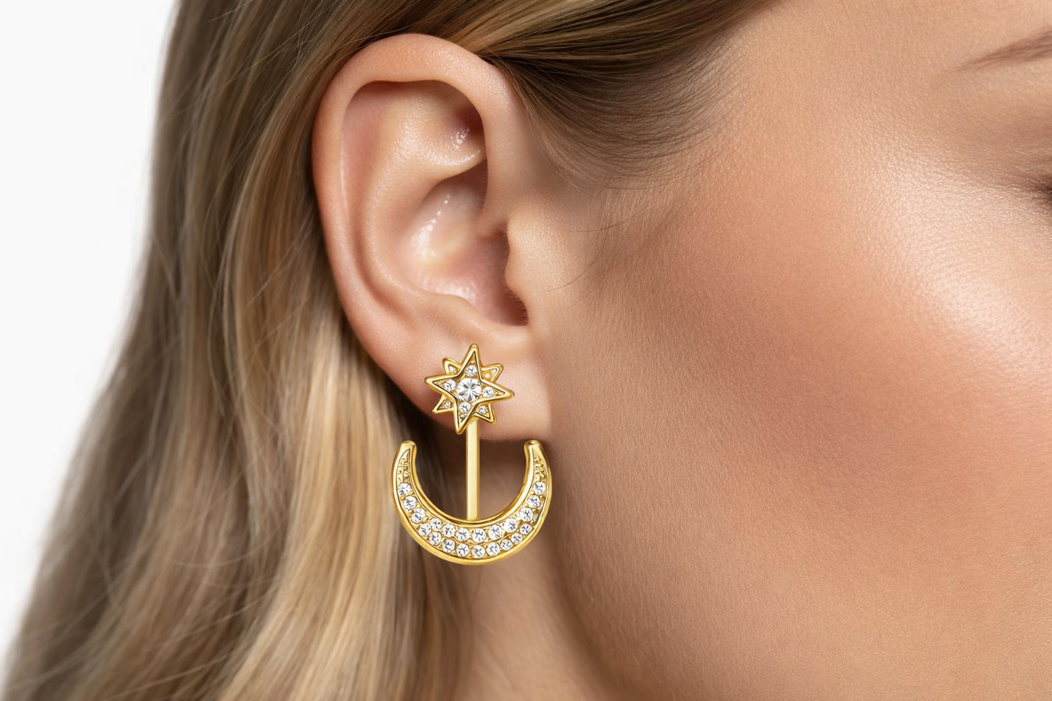 Brinco dourado com estrela e meia-lua com pedras brilhantes na orelha de mulher