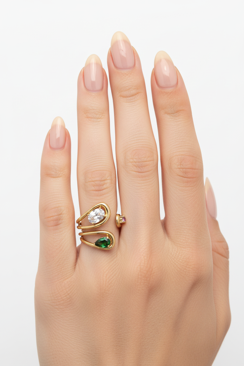 Mão feminina com unhas naturais e anel em ouro com pedras verdes e transparentes