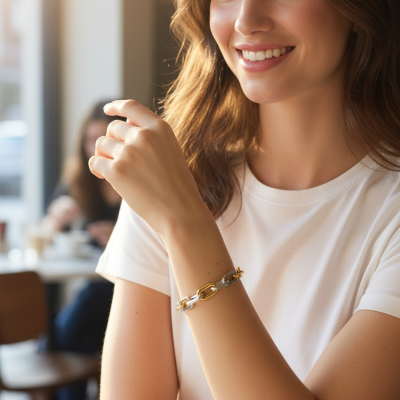 Mulher sorridente com pulseira de elos dourados e prateados no pulso, vestindo t-shirt branca, em café