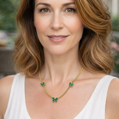 Colar dourado com três borboletas verdes no pescoço de mulher com camisa branca.