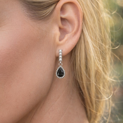 Brinco pendente com pedras negras e pérolas na orelha de mulher loira