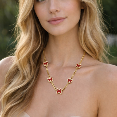 Colar dourado com borboletas vermelhas em mulher loira com vestido bege