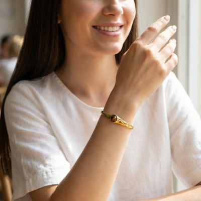 Mulher com pulseira dourada com pedra castanha usada no pulso esquerdo