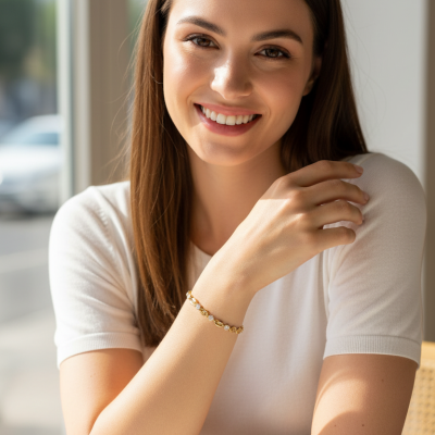Pulseira dourada com pedras claras no pulso de mulher com camisola branca junto a mesa com café