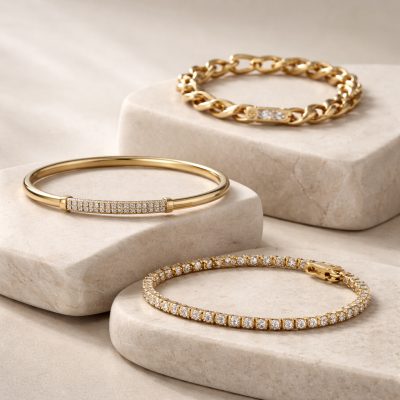 Três pulseiras douradas com pedras sobre blocos de pedra bege