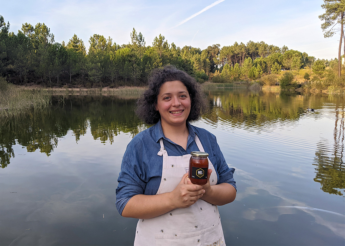 Mulher com avental segurando frasco de vidro em frente a lago com árvores