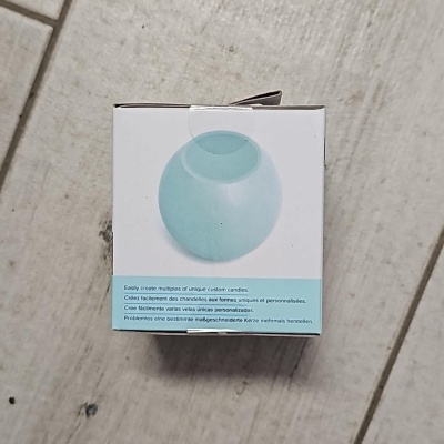 Caixa branca com vela redonda azul claro e texto em vários idiomas