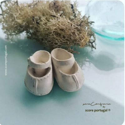 sapatinhos brancos de bebé em tecido ou pele com costuras e raminho seco ao fundo