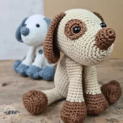 Dois cães de peluche de croché, um bege e castanho e outro branco e cinzento, sobre mesa de madeira