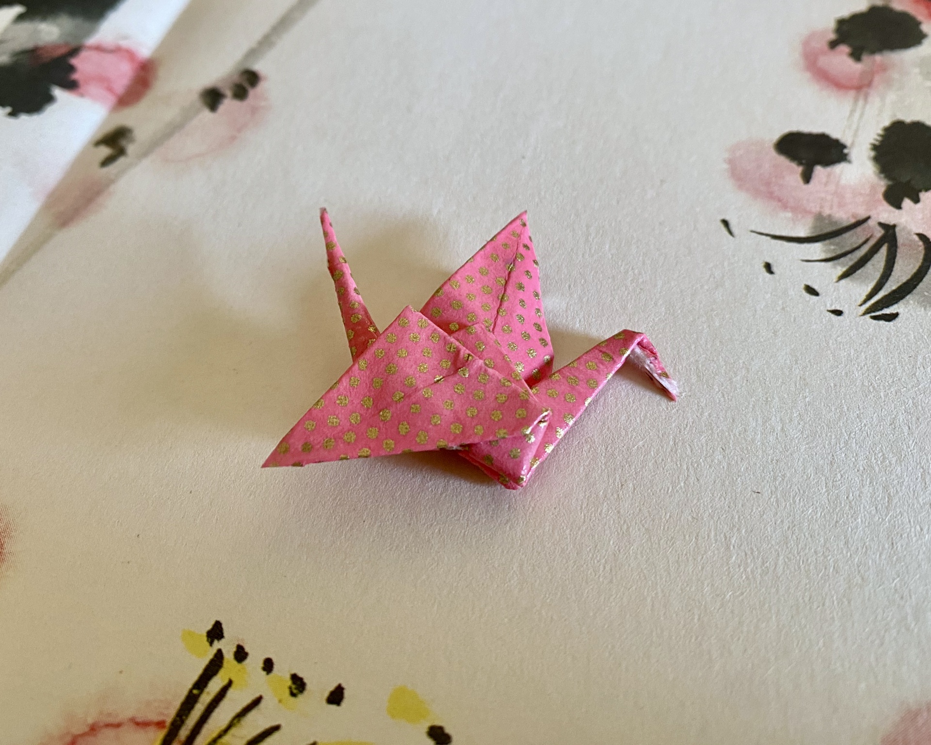 Pregadeira Tsuru Origami de pássaro rosa com bolinhas douradas sobre papel com estampas florais