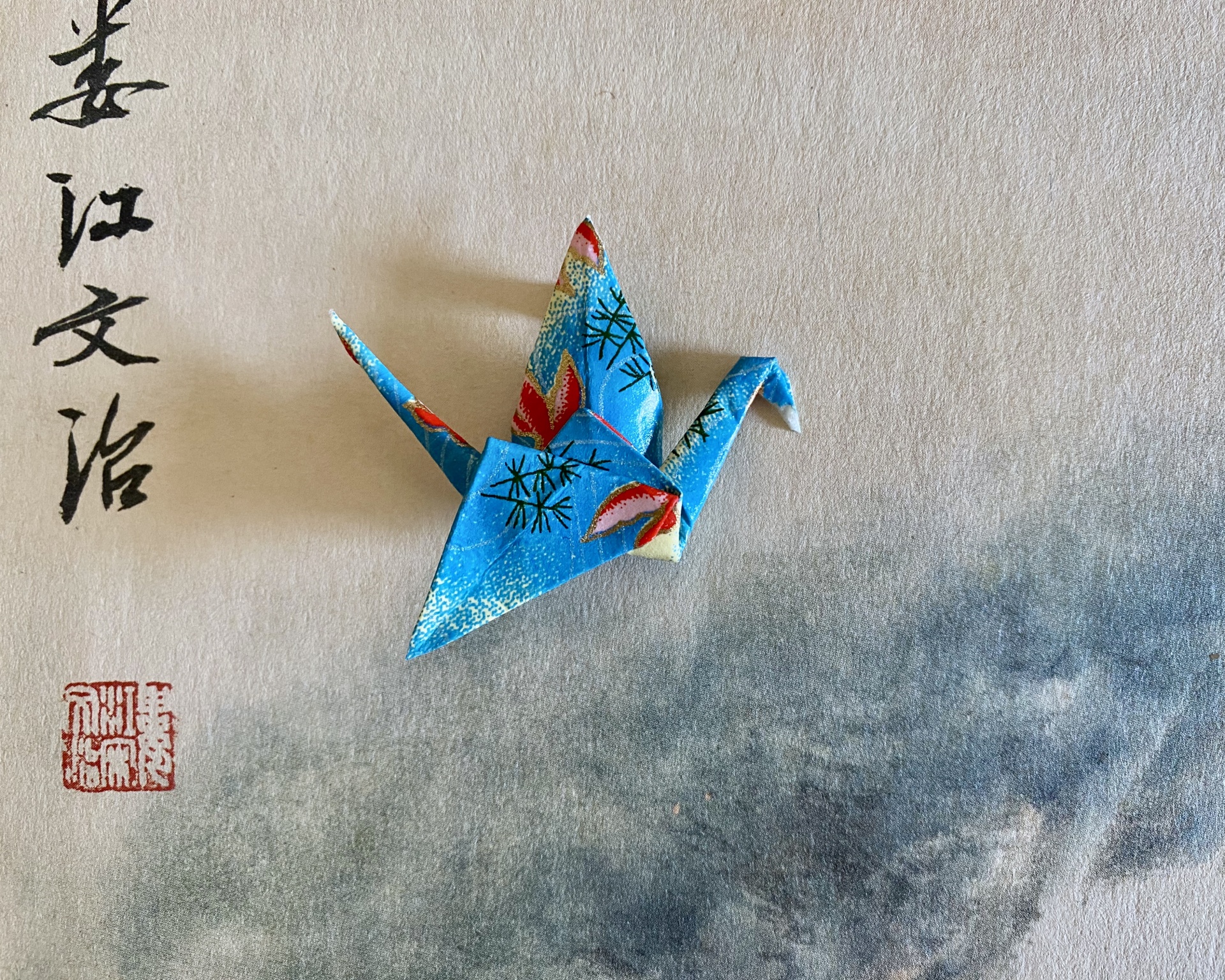 Pregadeira Tsuru Grou de origami azul com padrões sobre papel com caligrafia asiática e selo vermelho