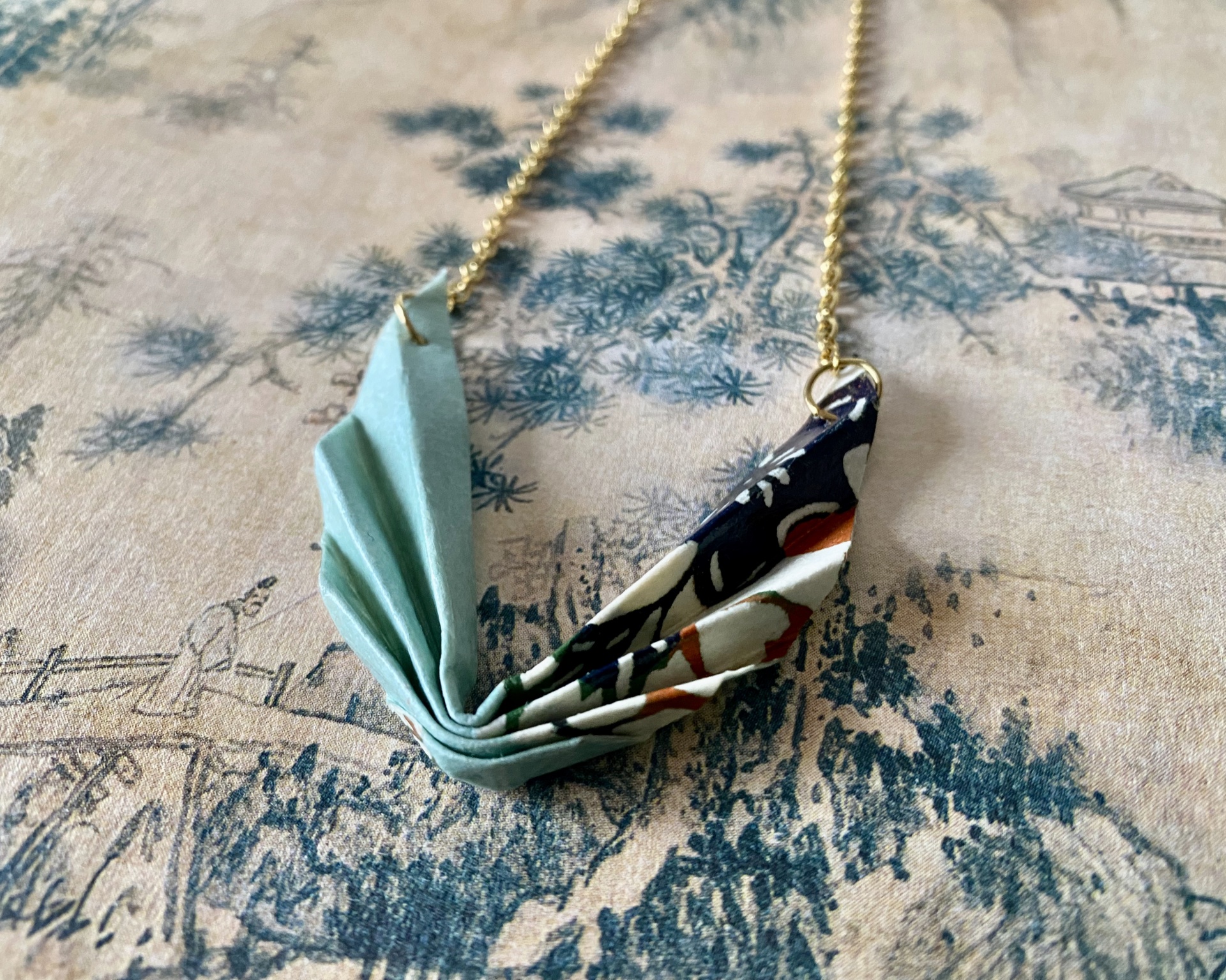 Colar Niki Colar com pendente dobrado azul e floral sobre fundo texturizado azul