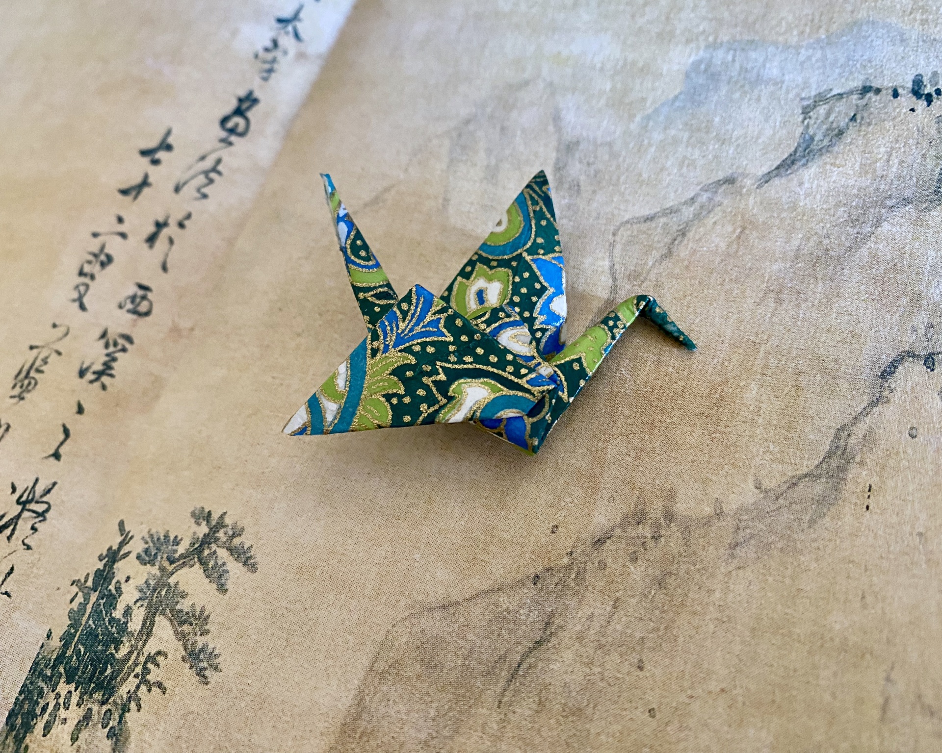 Pregadeira Tsuru Cisne de origami colorido sobre papel com texto asiático e ilustração.