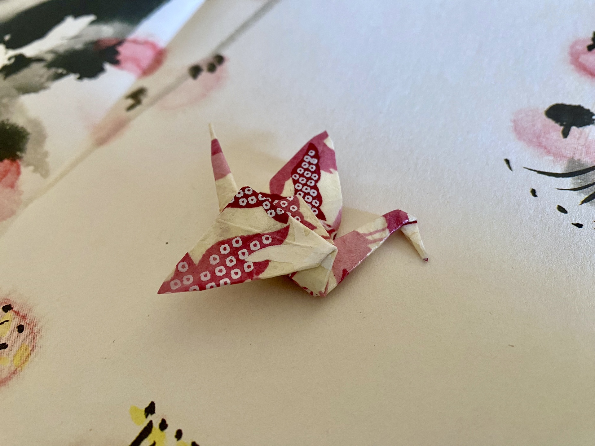 Pregadeira Tsuru Origami de pássaro em papel vermelho e branco sobre superfície branca com padrões florais