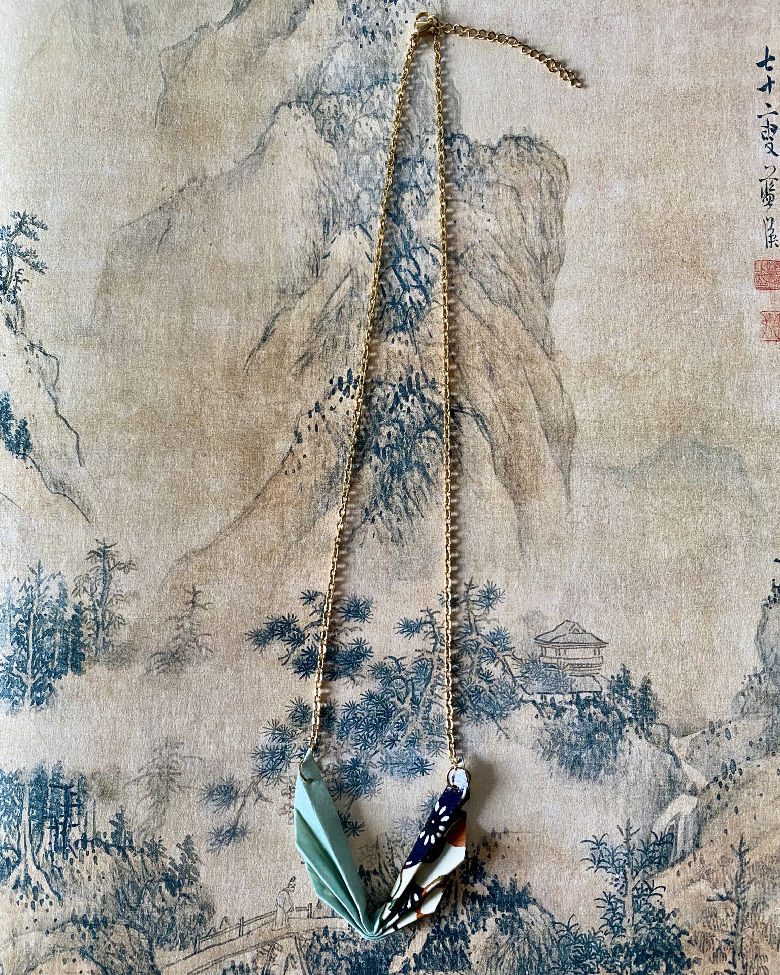 Colar Niki Colar com pendente em tecido estampado sobre fundo com pintura de paisagem asiática.