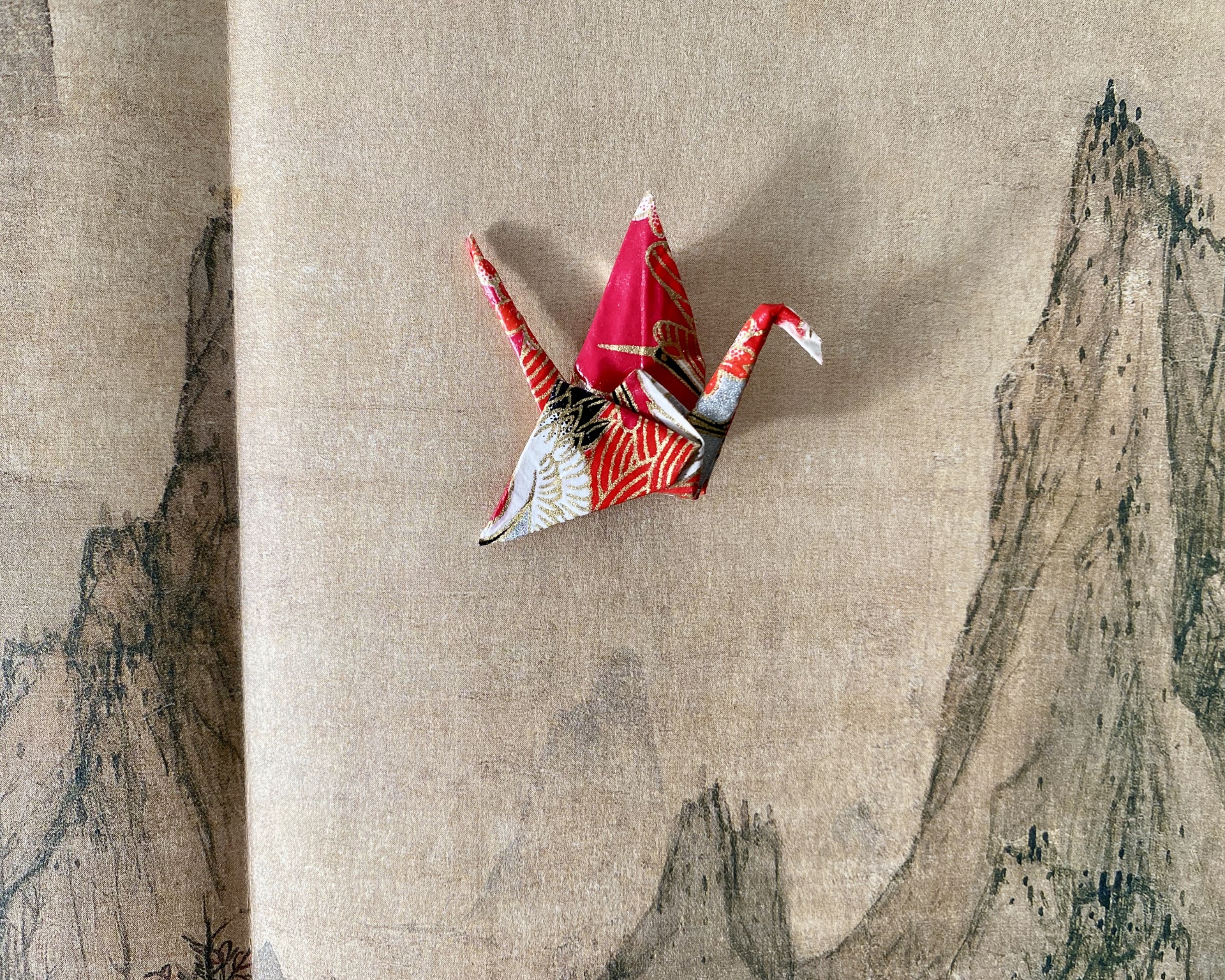 Pregadeira Tsuru Moinho de papel origami multicolorido sobre tecido bege com desenho de montanhas