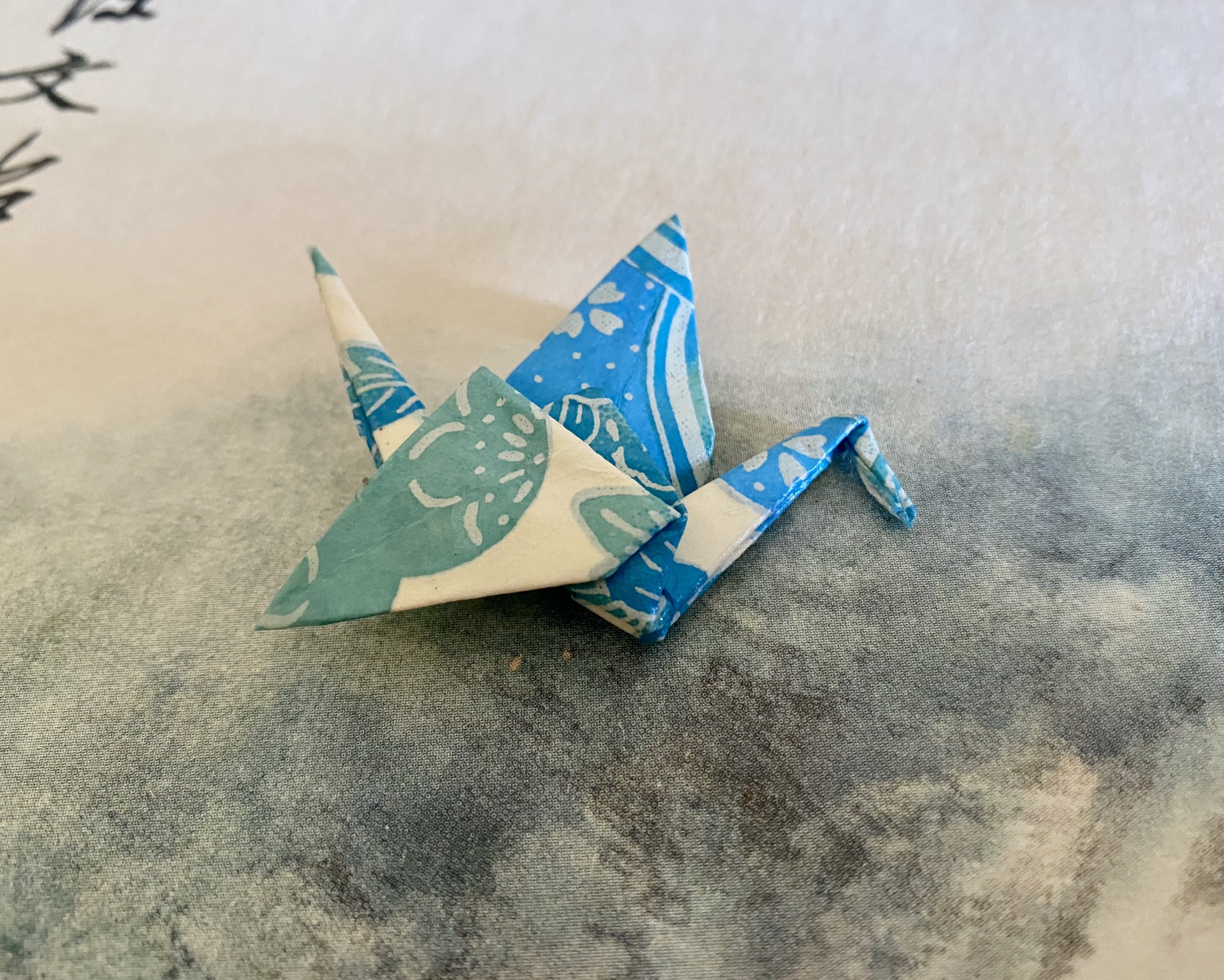 Pregadeira Tsuru Origami de papel azul com padrão floral sobre superfície cinza