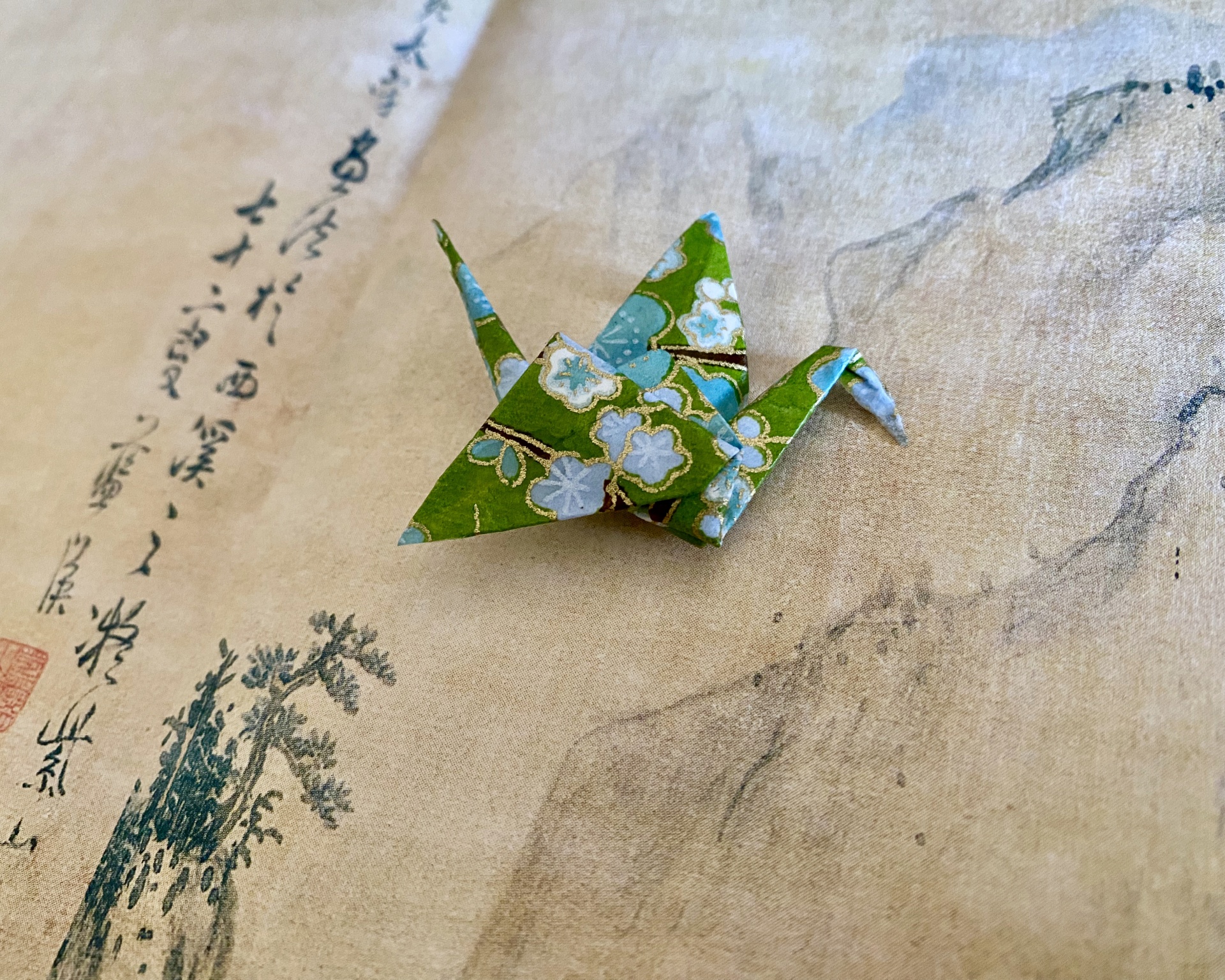 Pregadeira Tsuru Origami pássaro verde com padrão floral sobre papel com escrita oriental e desenho.