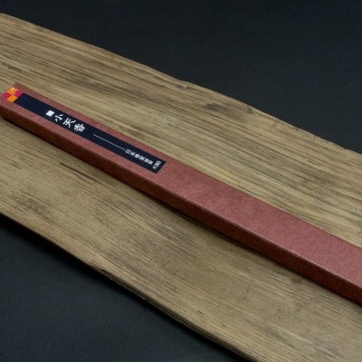 Estojo castanho comprido sobre tabuleiro de madeira claro, fundo preto.