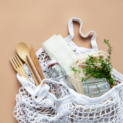 Saco de rede branco com frascos de vidro, talheres de madeira, pano branco e plantas verdes