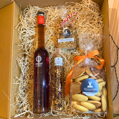 Caixa de presente com licor, granola, tisana e bolachas sobre palha.