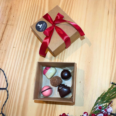 Caixa de bombons com fita vermelha e etiqueta, sobre mesa de madeira clara