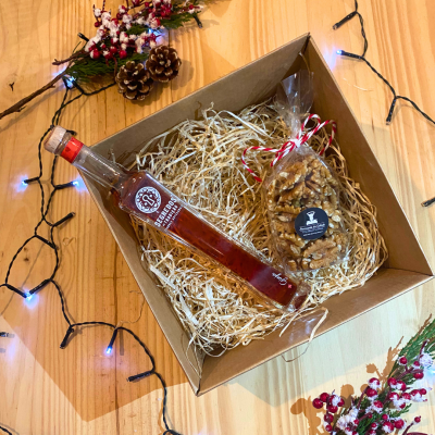 Caixa de presente com garrafa de licor e saco de nozes em palha dentro de caixa de cartão.