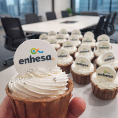 Cupcake com cobertura branca e etiqueta com logo enhesa. em mesa de escritório