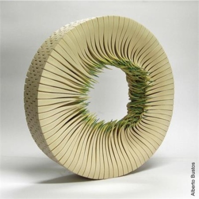 Objeto circular creme e verde com fendas finas num fundo cinzento claro.