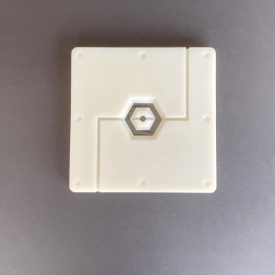 Produto quadrado branco com recorte hexagonal ao centro sobre superfície cinzenta