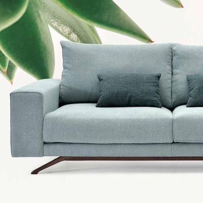 Sofá azul com almofadas escuras e folhas verdes ao fundo