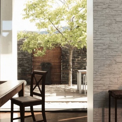 Sala de jantar em madeira com parede revestida a pedra e vista para pátio exterior.