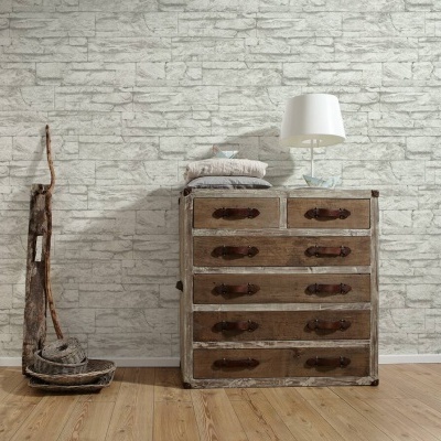 Cómoda vintage em madeira com gavetas e puxadores de couro, luminária branca e suporte rústico ao lado, parede de pedras brancas e chão de madeira clara