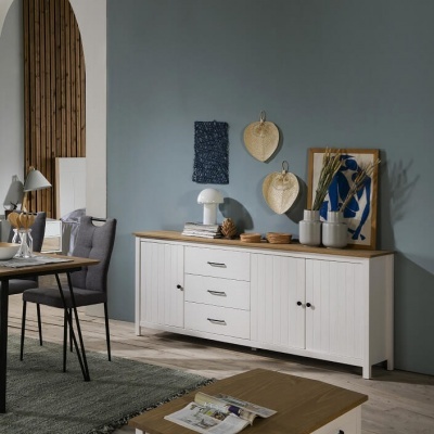 Aparador branco de madeira com decoração sobre ele, parede azul de fundo, mesa de jantar e cadeiras cinzentas ao lado